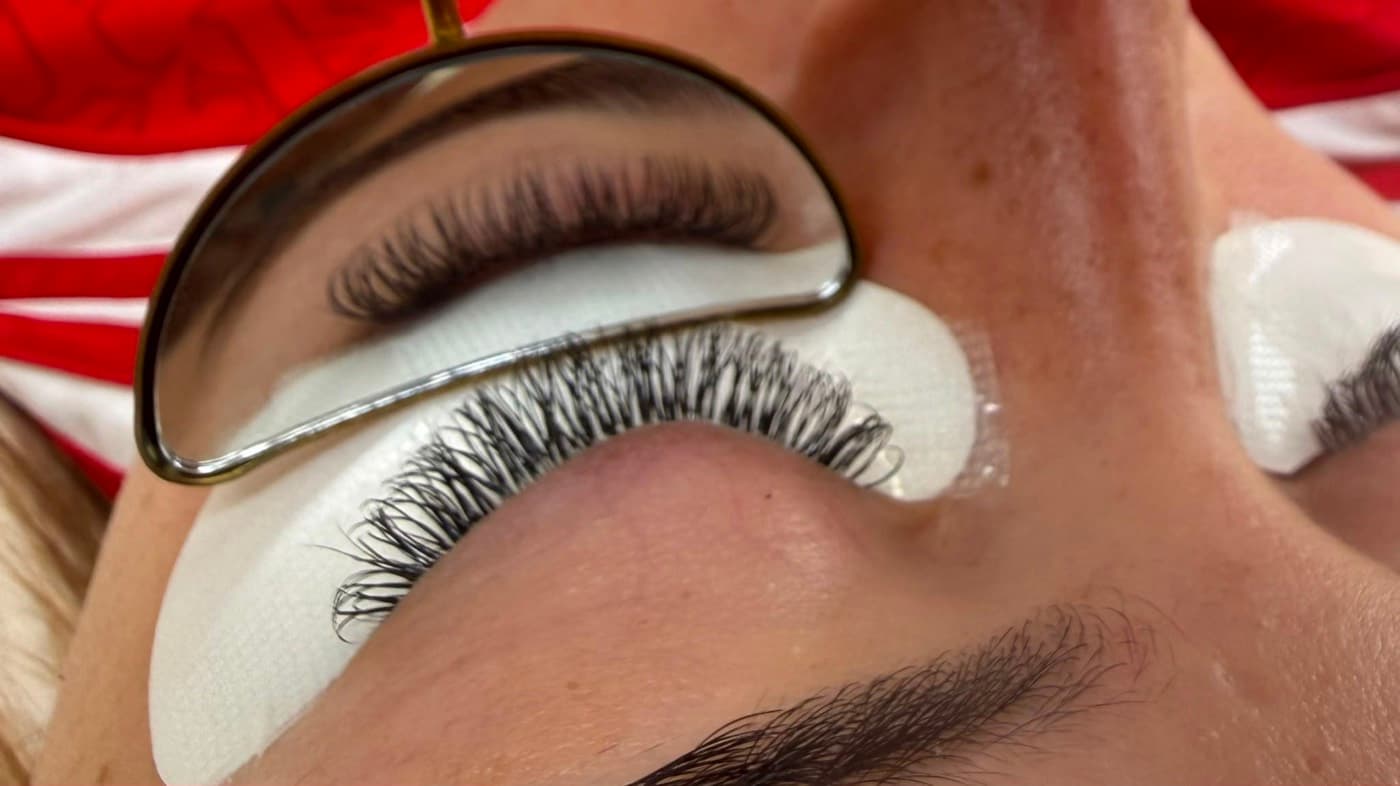 Classic lash extensions part-way through application, with the lash line checked in a mirror